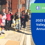 Text reads: "City of Seattle, 2023 Duwamish Valley Program Annual Update." A group of people stand outside near a crosswalk. One person has cut a ribbon tied to a pole.