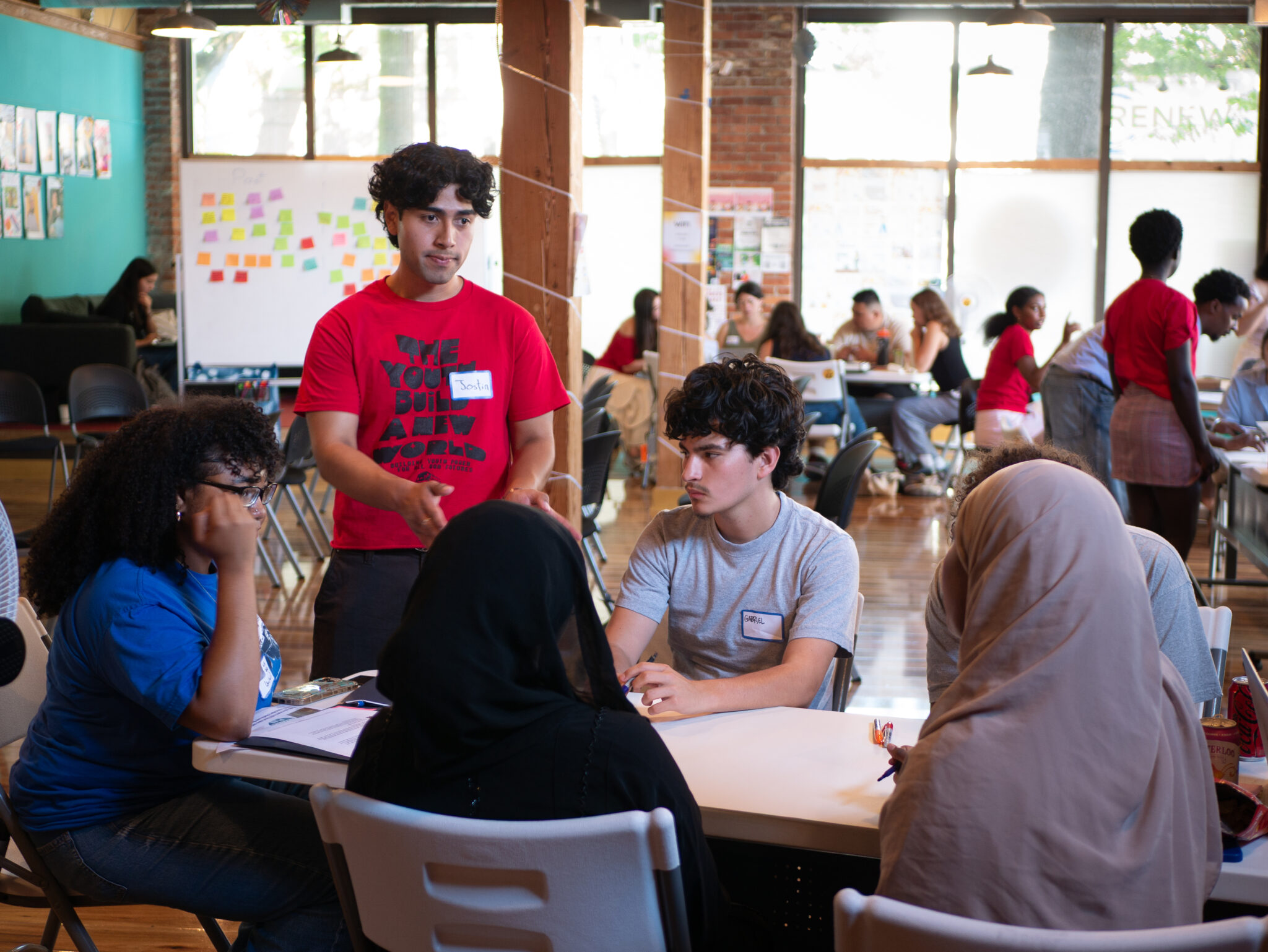 Jostin Cuenca standing wearing red and Kisaya Canada sitting wearing blue assisting participants.