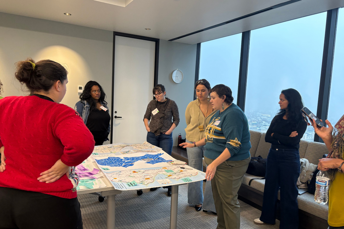 Vicky Murray, along with assembly participants, stands over a conference room table with a large map of Seattle.