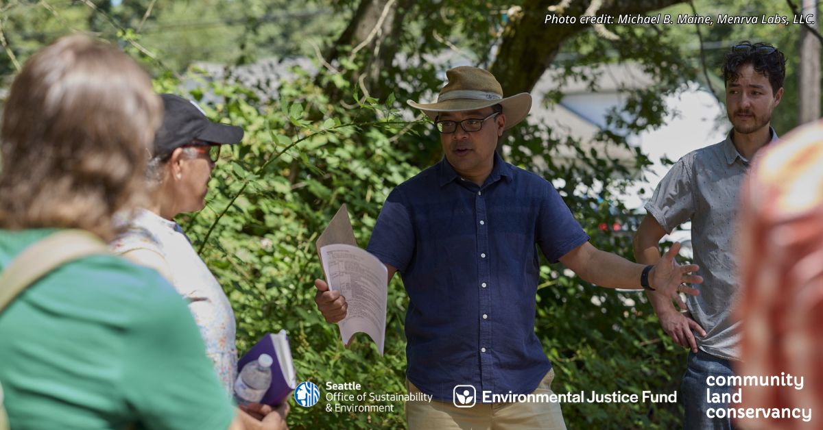 A few people outside are learning from an instructor standing in front of greenery. 