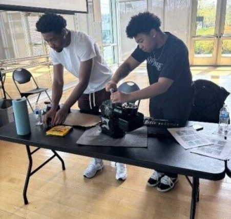 Two people stand behind a black table, fixing an appliance.