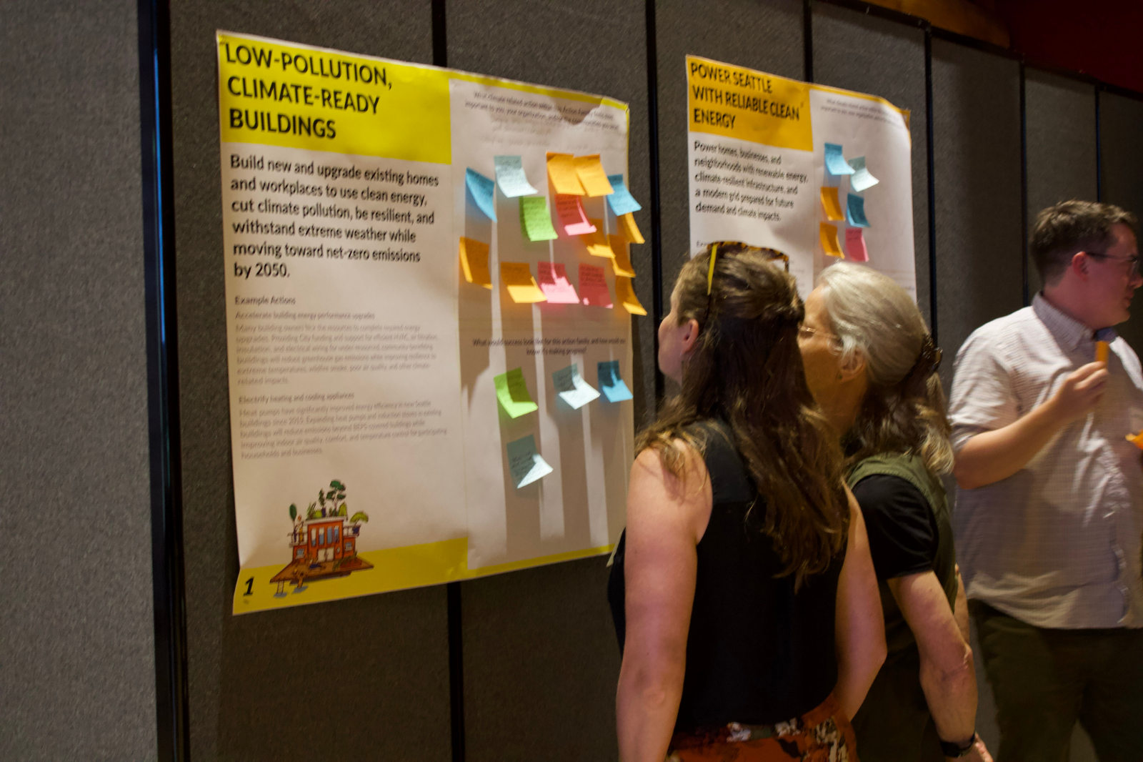 People reading sticky notes on climate action posters displayed on a wall.