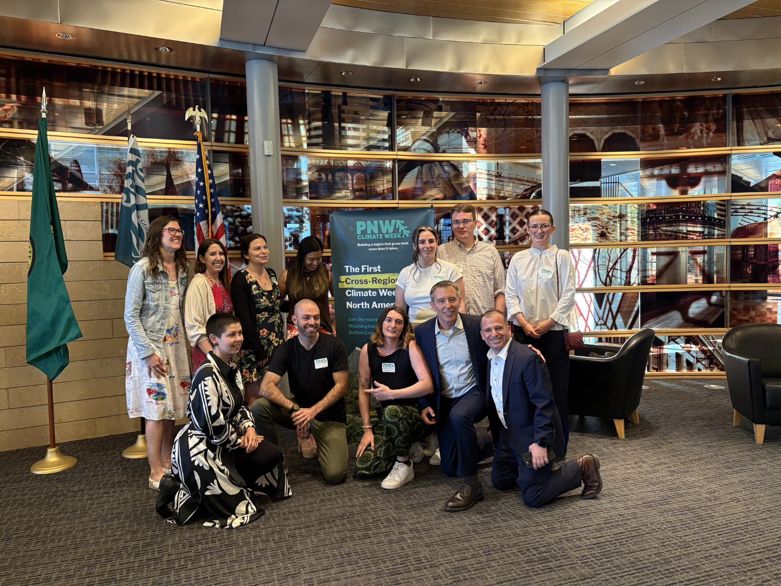 A group of people posing indoors in front of flags and a PNW Climate Week banner.