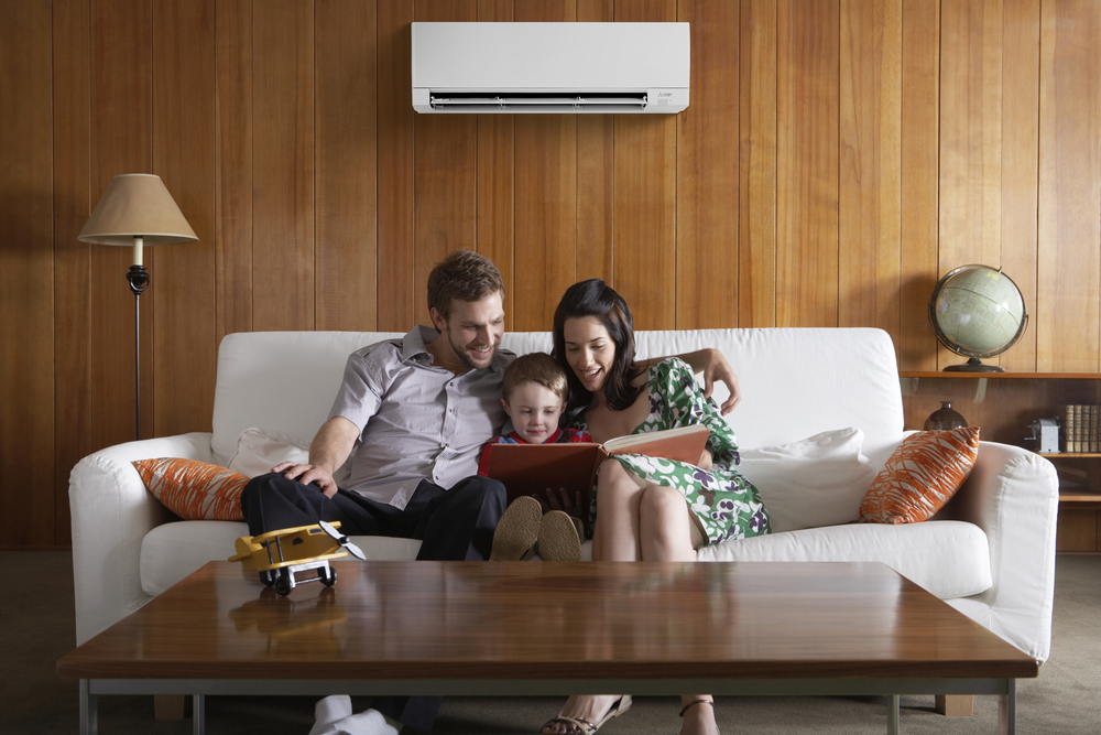 A family with a young child reads a book on a couch as a wall mounted heat pumps provides cooling. Credit: Mitsubishi Electric