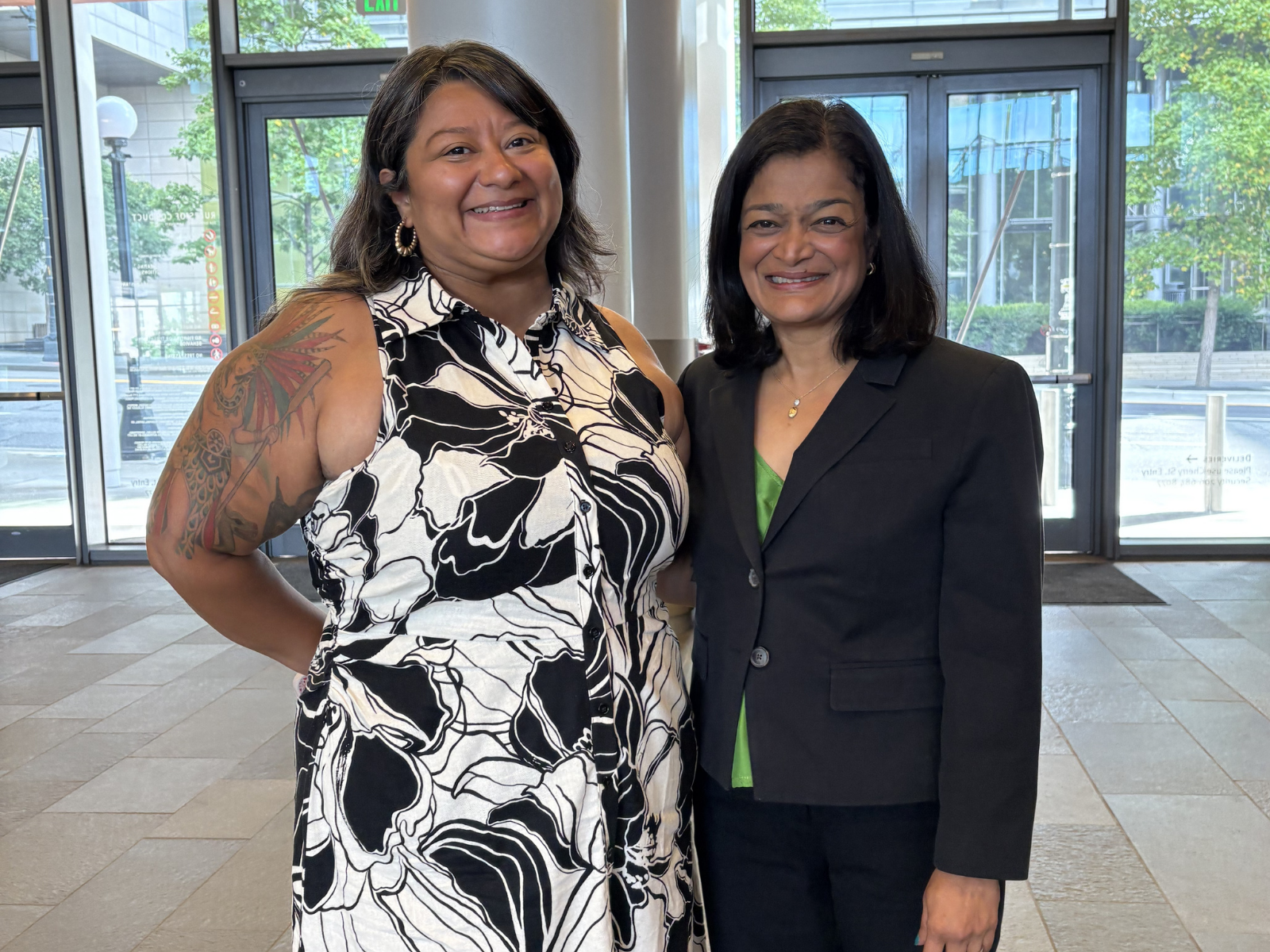 OSE Director Allala and Representative Jayapal standing together in a bright indoor lobby with large windows behind the