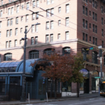 Red-brick building with a covered transit station entrance and a city bus on the street.