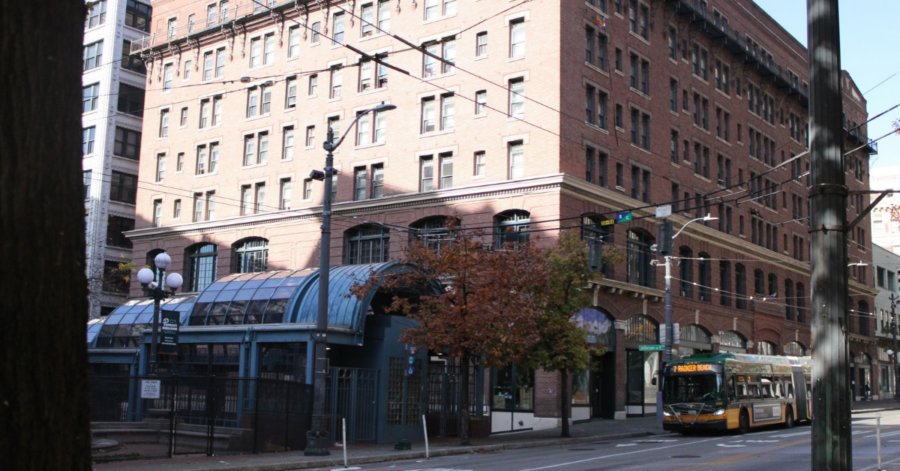 A brick building with a covered entrance to a public-transit station and a city bus on the street.